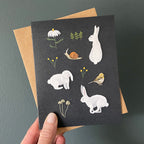 Greeting card with animal illustrations held by a hand against a dark background
