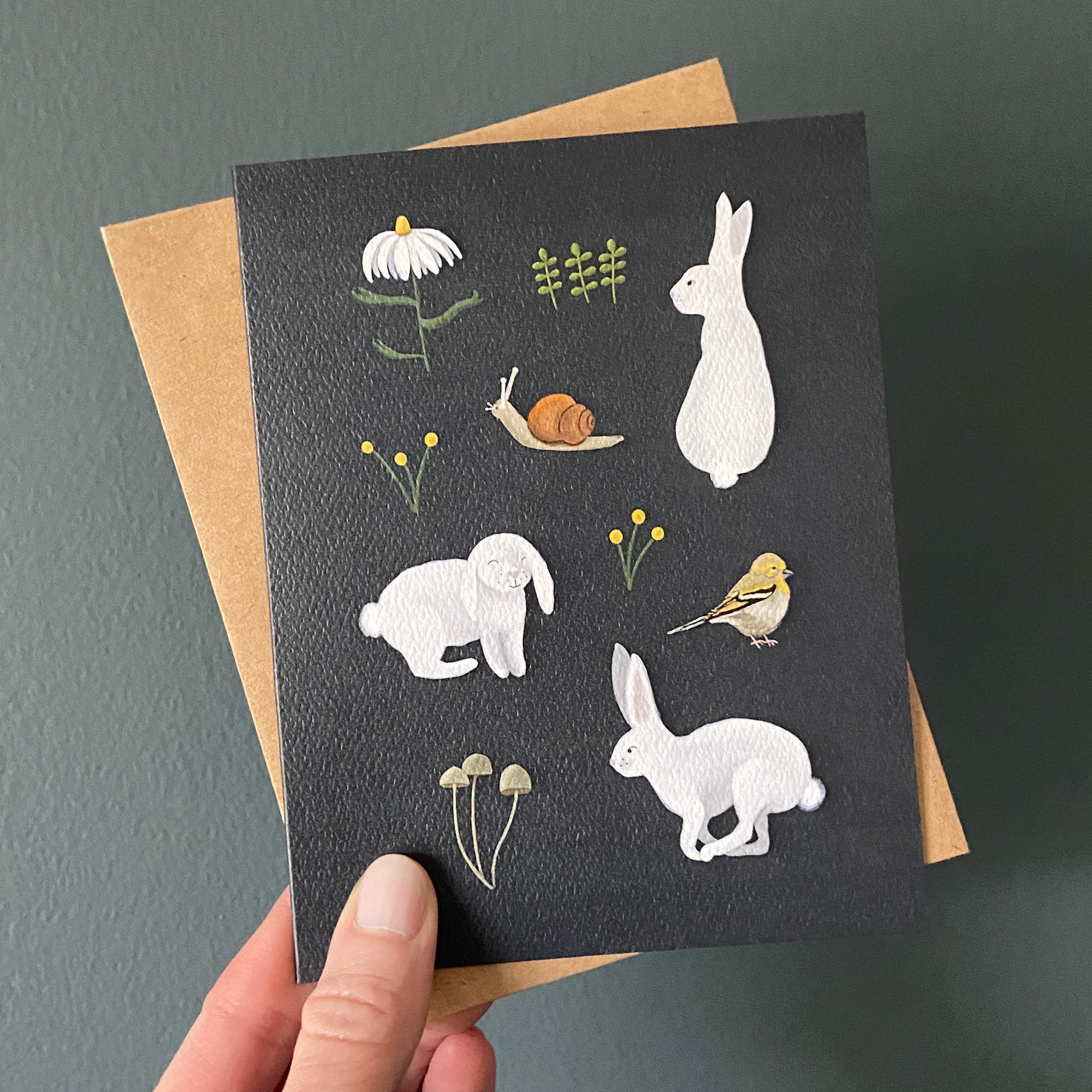 Greeting card with animal illustrations held by a hand against a dark background