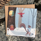 Whimsical holiday card with a winter scene featuring a squirrel, chipmunk and cardinal near a tree house.
