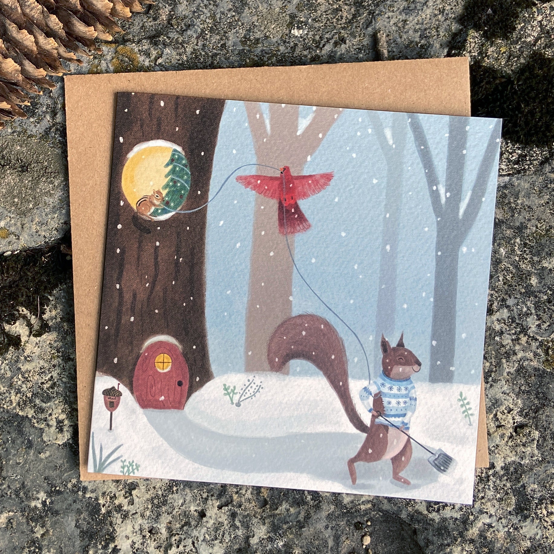 Whimsical holiday card with a winter scene featuring a squirrel, chipmunk and cardinal near a tree house.