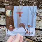 Illustrated holiday card with a squirrel and bird in a snowy forest, held over a natural stone background.