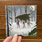 Illustration of rabbits carrying a Christmas tree in a snowy forest, held against a wooden background.