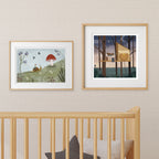 Two framed nursery artworks above a crib with a neutral wall background