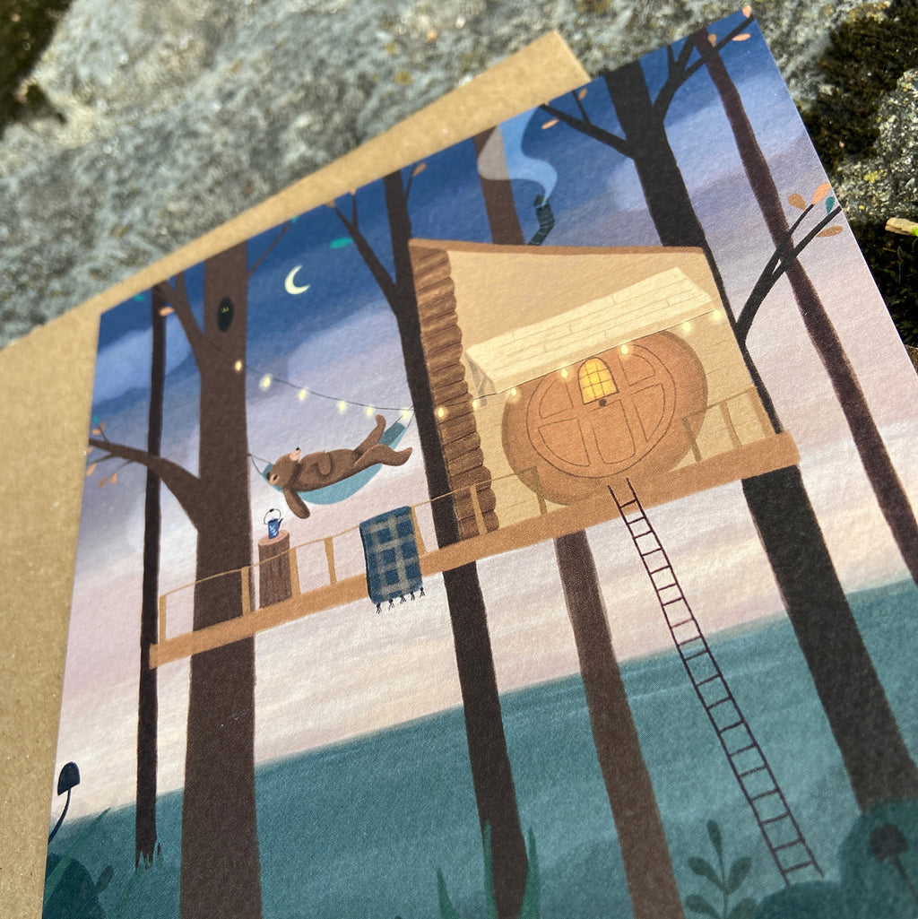 Illustrated card featuring a treehouse in a forest with a ladder and bear relaxing in a hammock, on a textured surface.