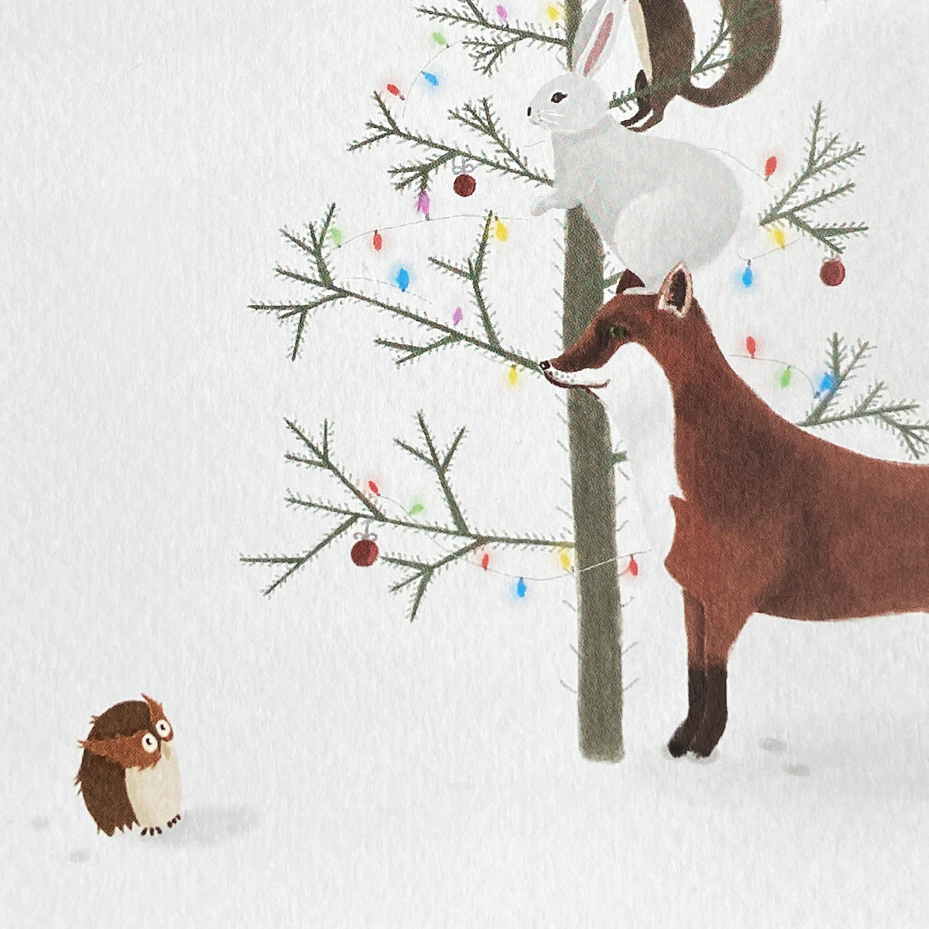 Christmas card illustration of a fox, rabbit, and owl by a decorated tree in the snow.